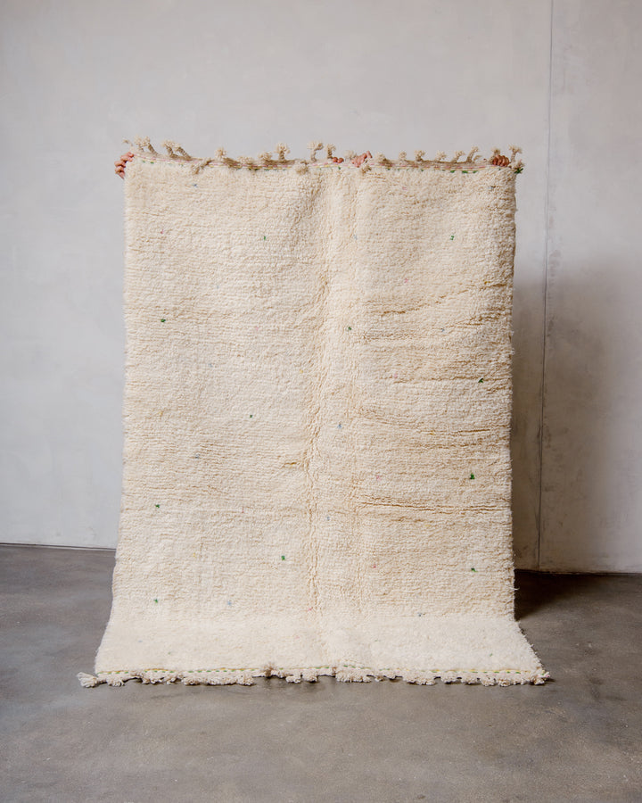 Berberlin Beniourain rug in cream wool with coloured dots being held up in front of a white wall. 