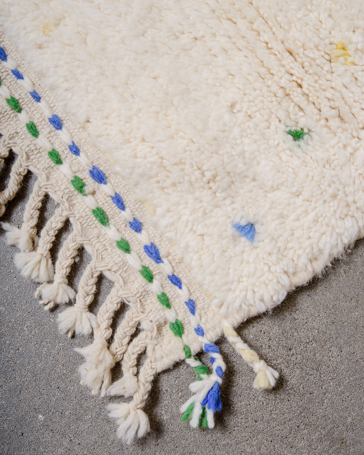 Corner detail of rug showing blue and green dashed details in the woven end and natural wool tassels.