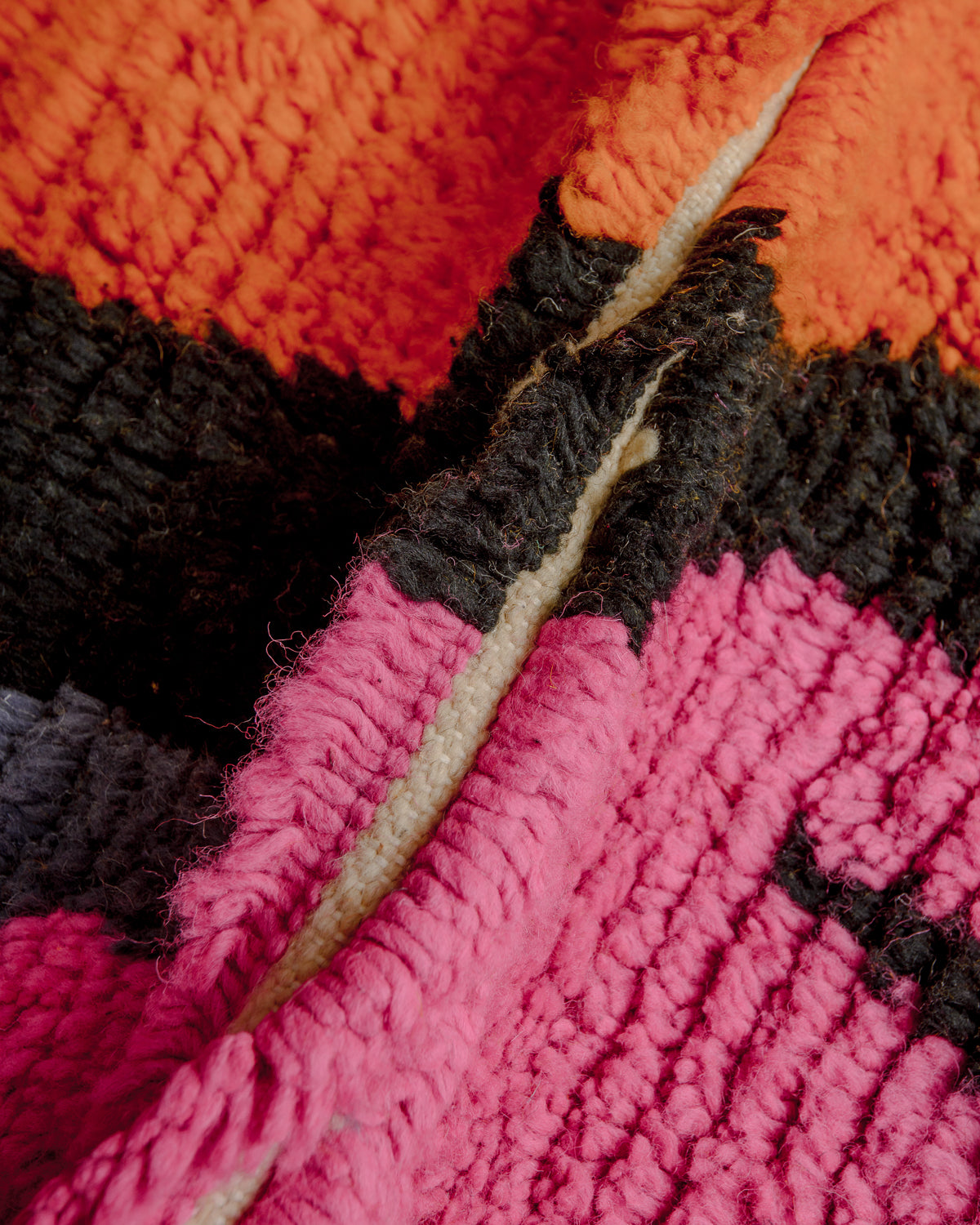 Close up of wool rug with pink, black and orange wool.