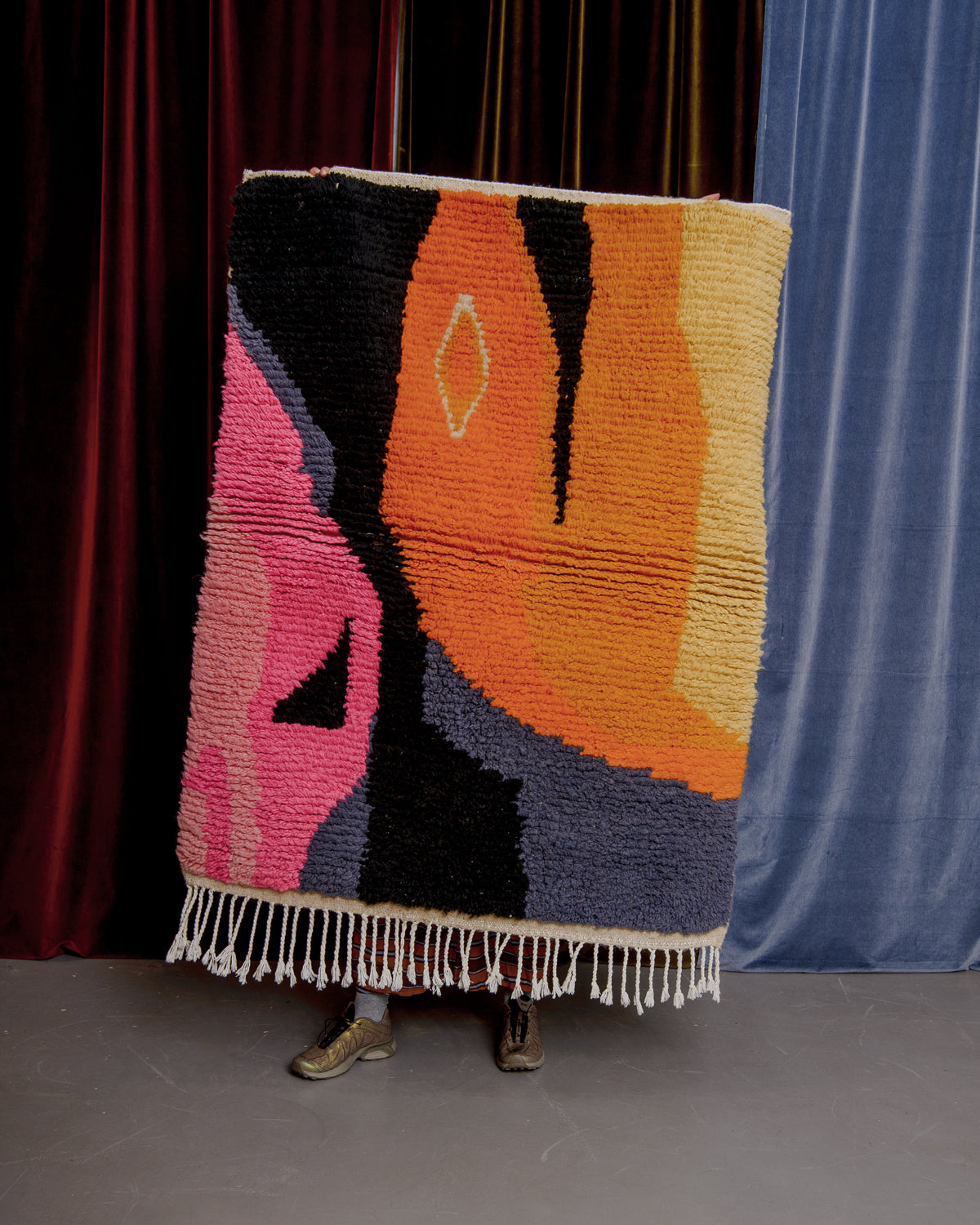 Vintage boujaad rug held in front of velvet curtains.