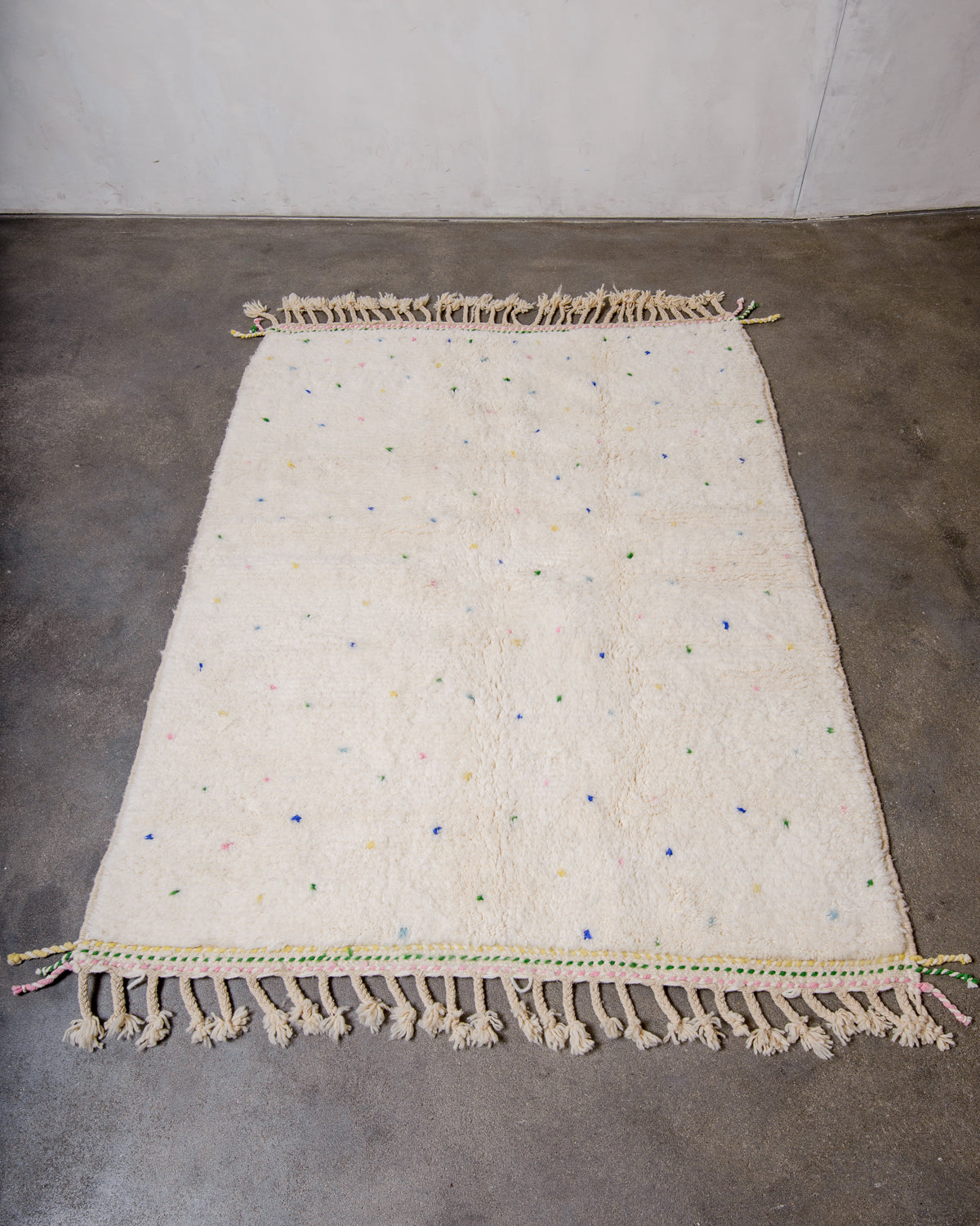 Berberlin Beniourain rug in cream wool with colourful dots laying on concrete floor.
