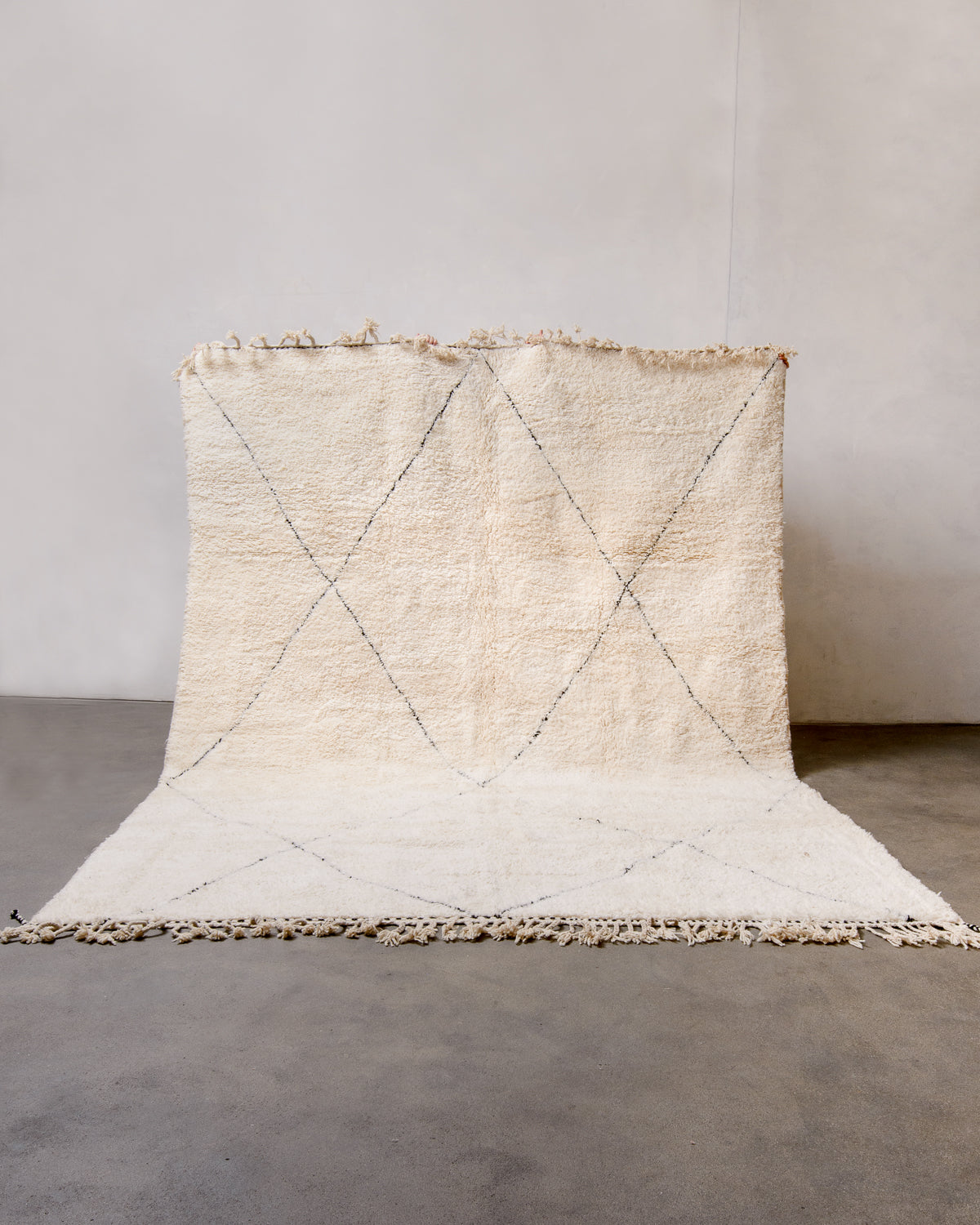 Cream Berber rug with black diamond design being held up in front of white wall. 