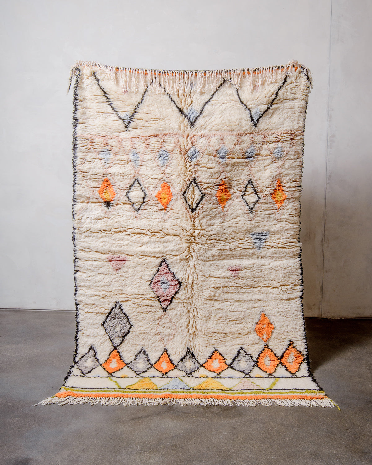 Berberlin Finest Rug in plush cream wool with a design made up of zigzags and diamonds being held up in front of a white wall. 