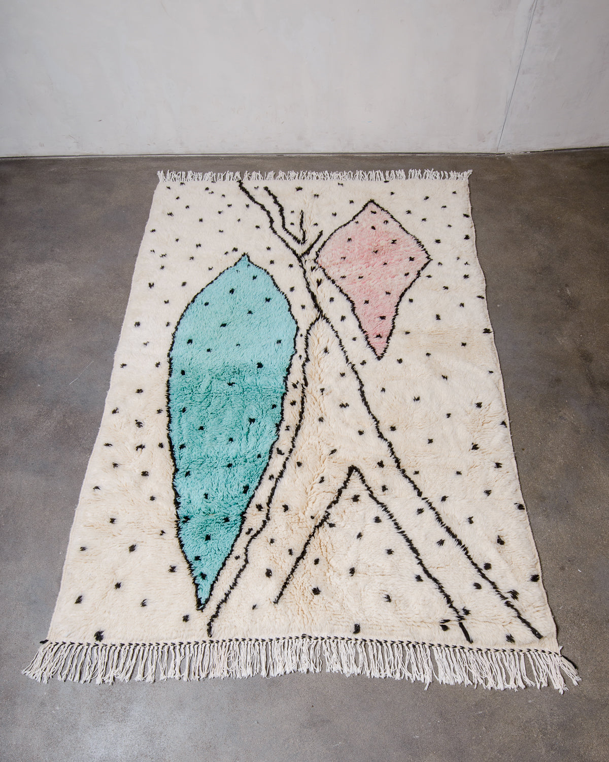 Berberlin Finest Rug made of plush cream wool with a cool design in including large pink and turquoise forms, and black polka dots, laying flat on concrete studio floor.