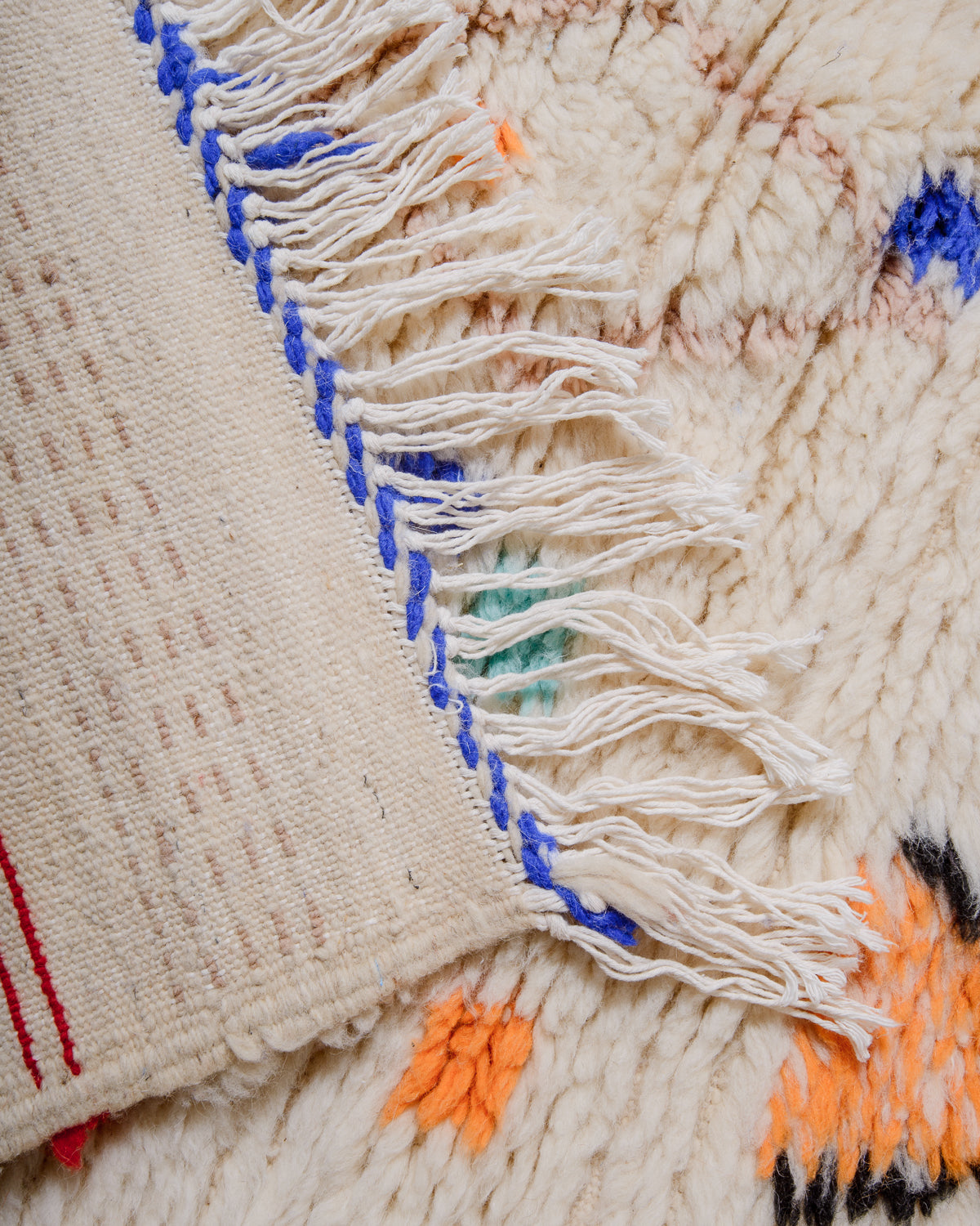 Folded corner of rug made of thick, fluffy wool pile with white cotton tassels. 