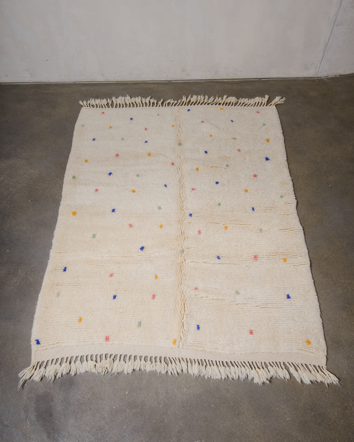 Cream wool rug with colourful polka dots on a concrete floor.