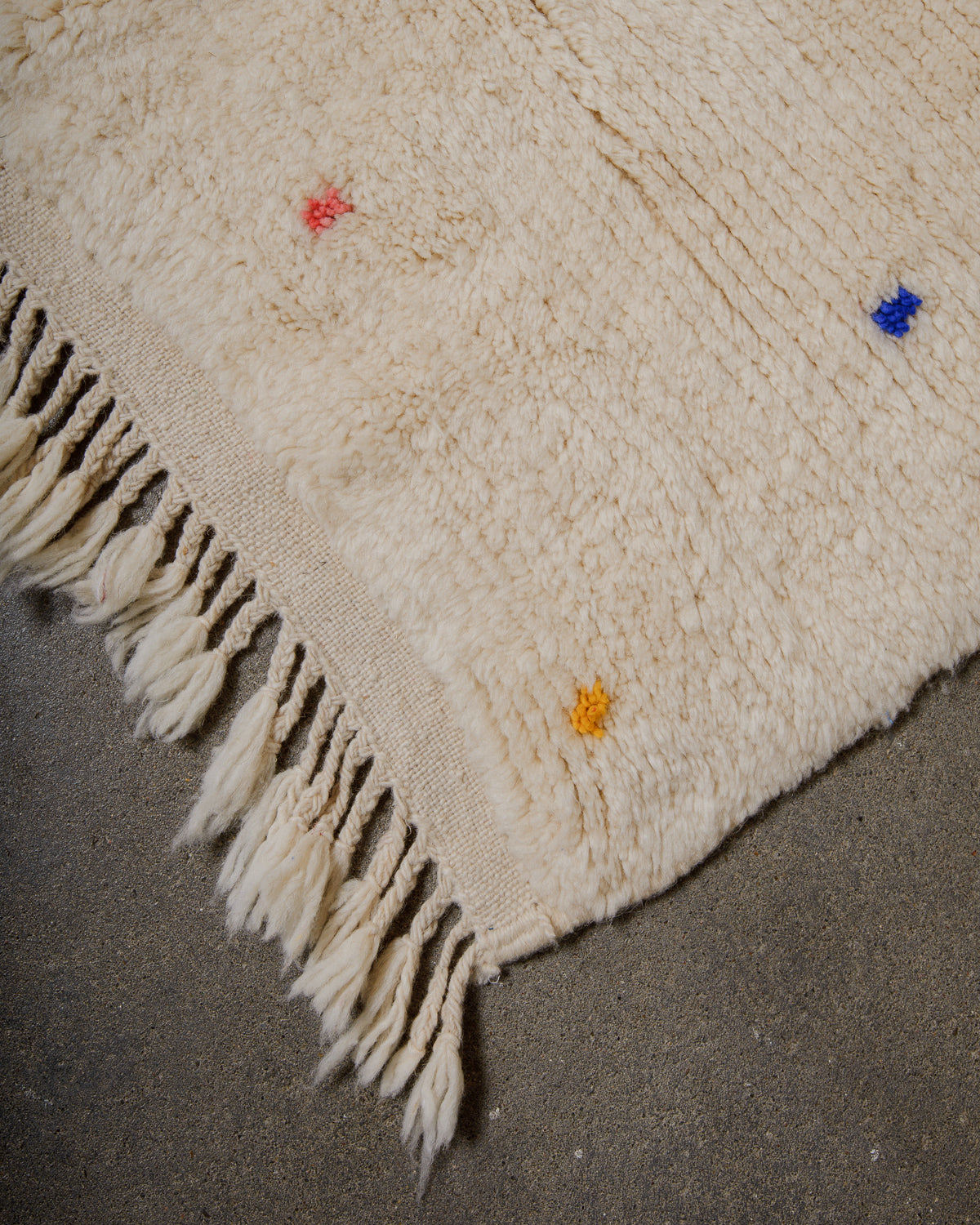 Corner of cream wool rug with colourful polka dots and natural wool tassels.