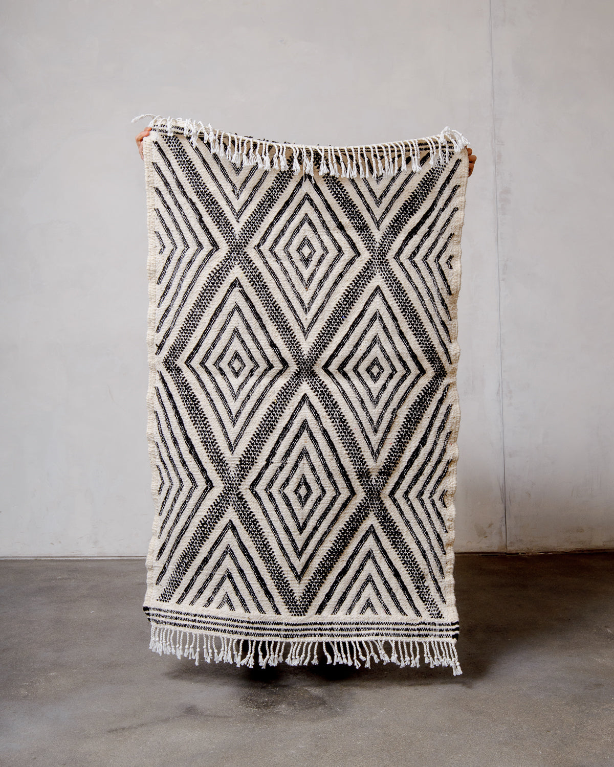 Small Berberlin Kelim Rug in black and white being held up in front of a white wall.