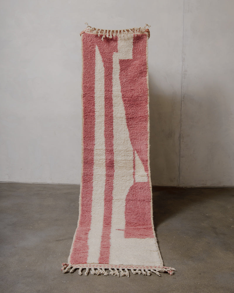 Pink and white woven rug with tassels on a plain floor.