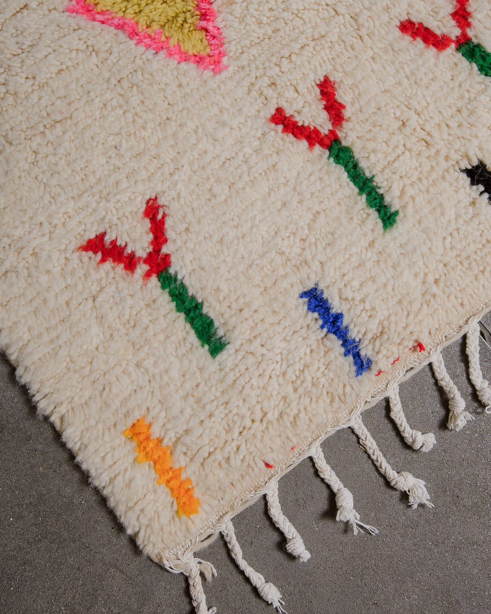 Corner of azilal rug with white cotton tassels on concrete floor. 