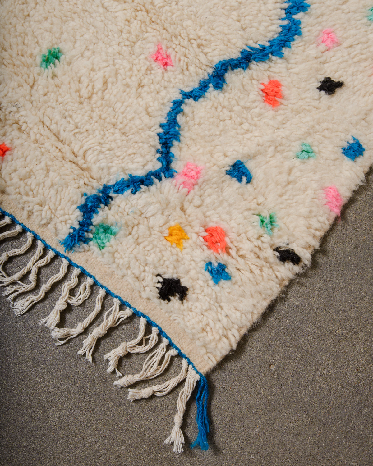 Corner of Azilal run with cream wool and colourful design and white cotton tassels across the edge with blue trim.