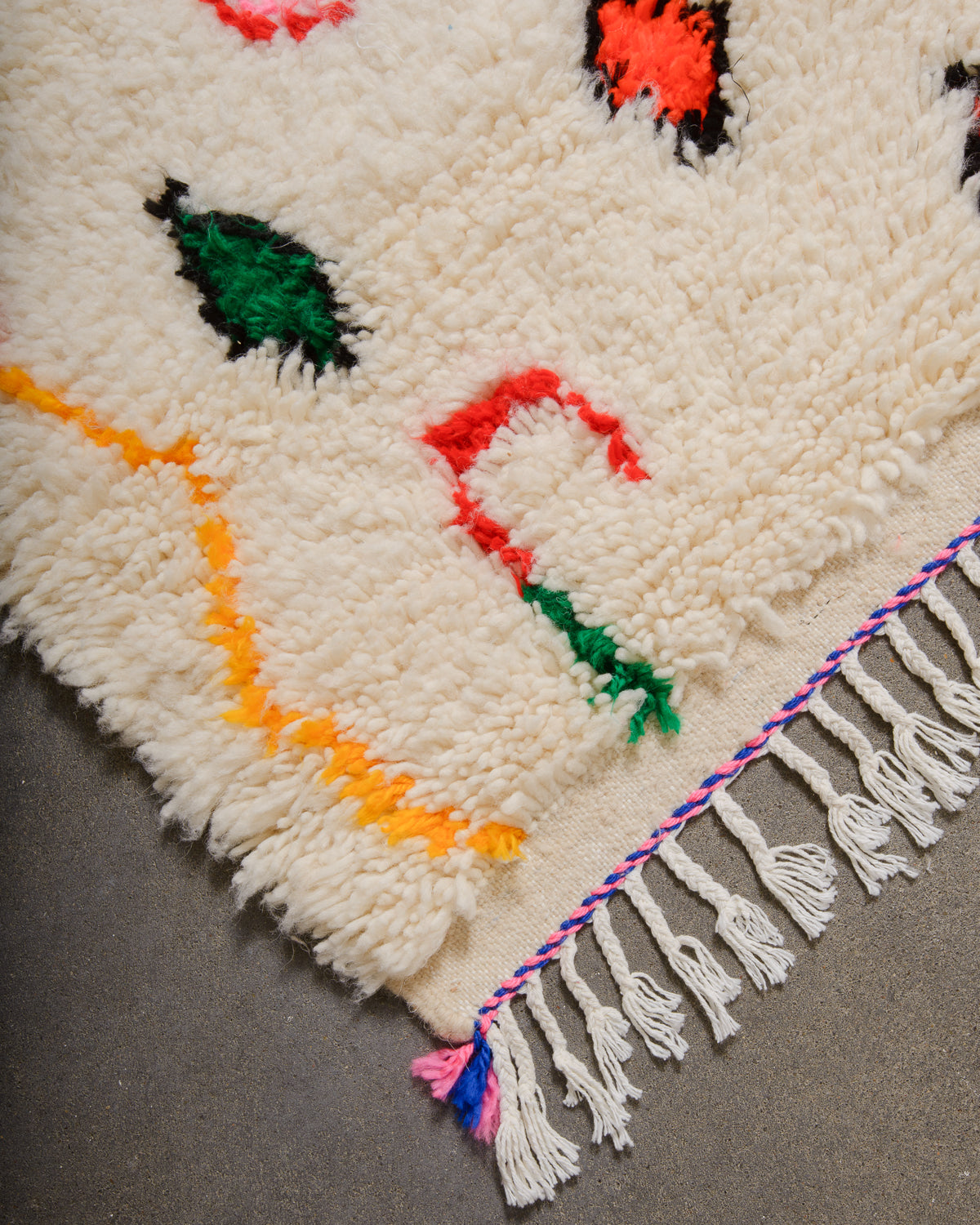 Corner of Azilal rug with a tightly woven edge and white cotton tassels along the end.