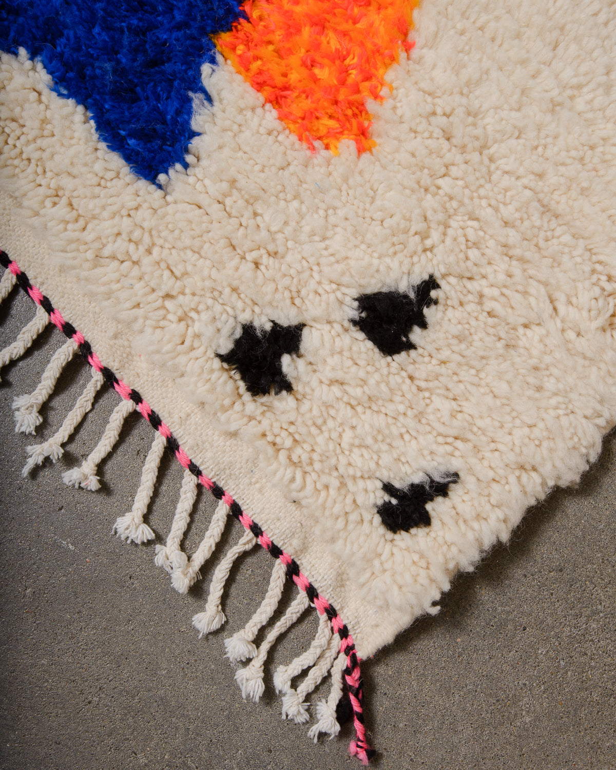 Corner of Azilal rug with a tightly woven edge and white cotton tassels along the end.