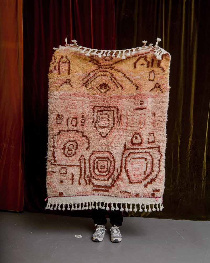 Berberlin Finest azilal rug in pink and orange, being held up in front of a wall of velvet curtains.