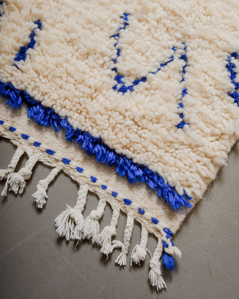 Corner of Berberlin Azilal rug with cream and blue design and white cotton tassels.