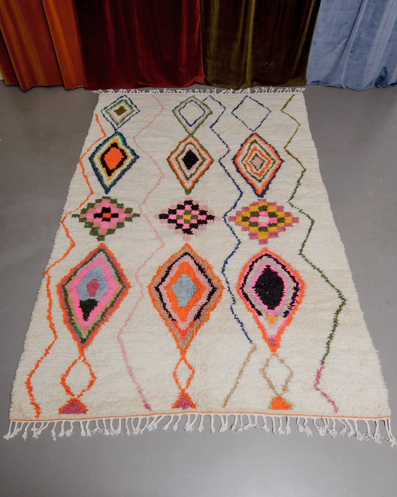 Colourful azilal rug featuring pink, orange and olive on a grey floor.
