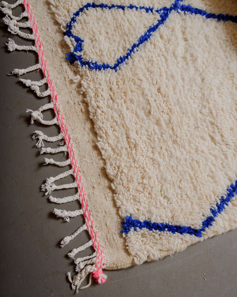 Corner of azilal rug with pink stitching along the end and white cotton tassels. 