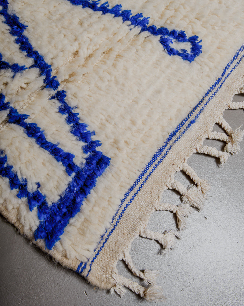 Corner of azilal rug with blue stitching and white cotton tassels. 
