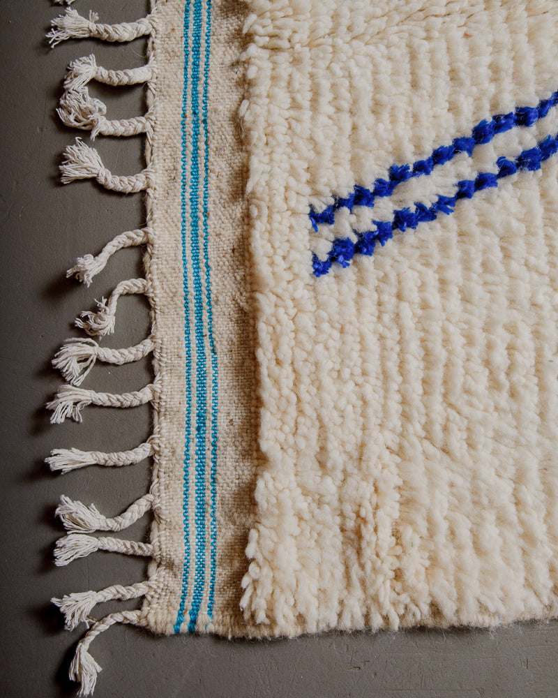 Corner of azilal rug with turquoise stitching and white cotton tassels. 