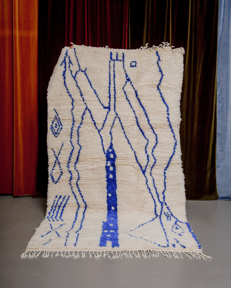 Colourful azilal rug held in front of velvet curtains. 