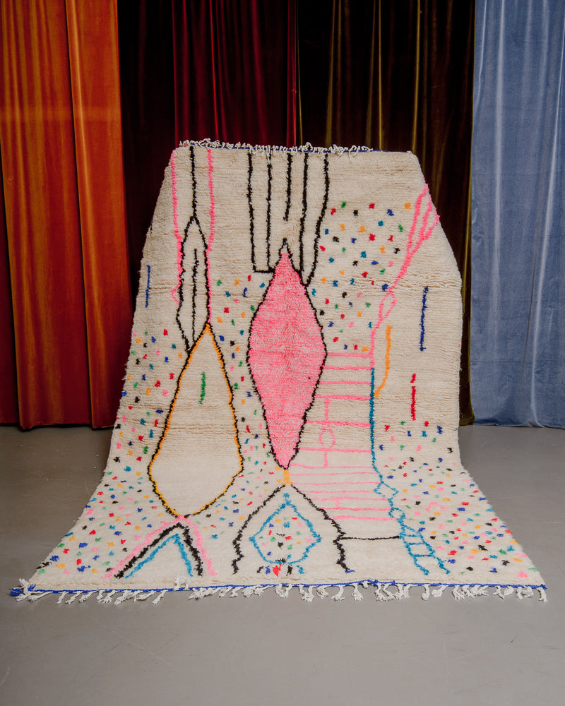 Colourful azilal rug held in front of velvet curtains. 