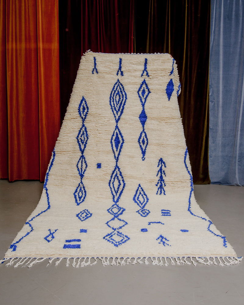 Cream and blue azilal rug held in front of velvet curtains. 