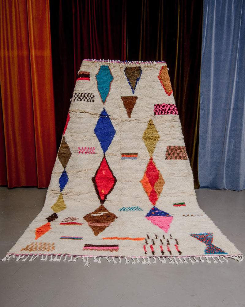 Colourful azilal rug held in front of velvet curtains. 