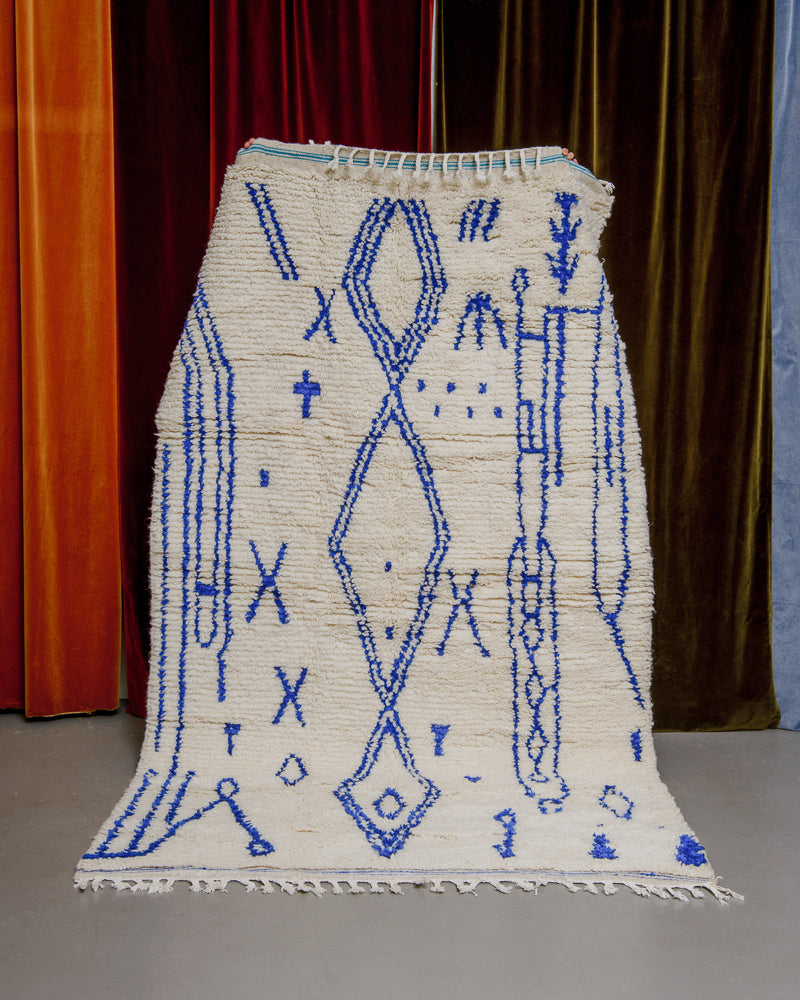 Colourful azilal rug held in front of velvet curtains. 