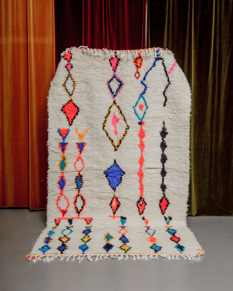 Colourful azilal rug held in front of velvet curtains. 