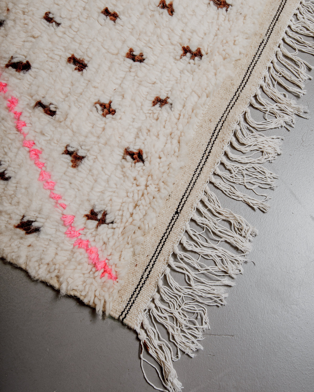 Edge of azilal rug with black stitching along the end and white cotton tassels. 