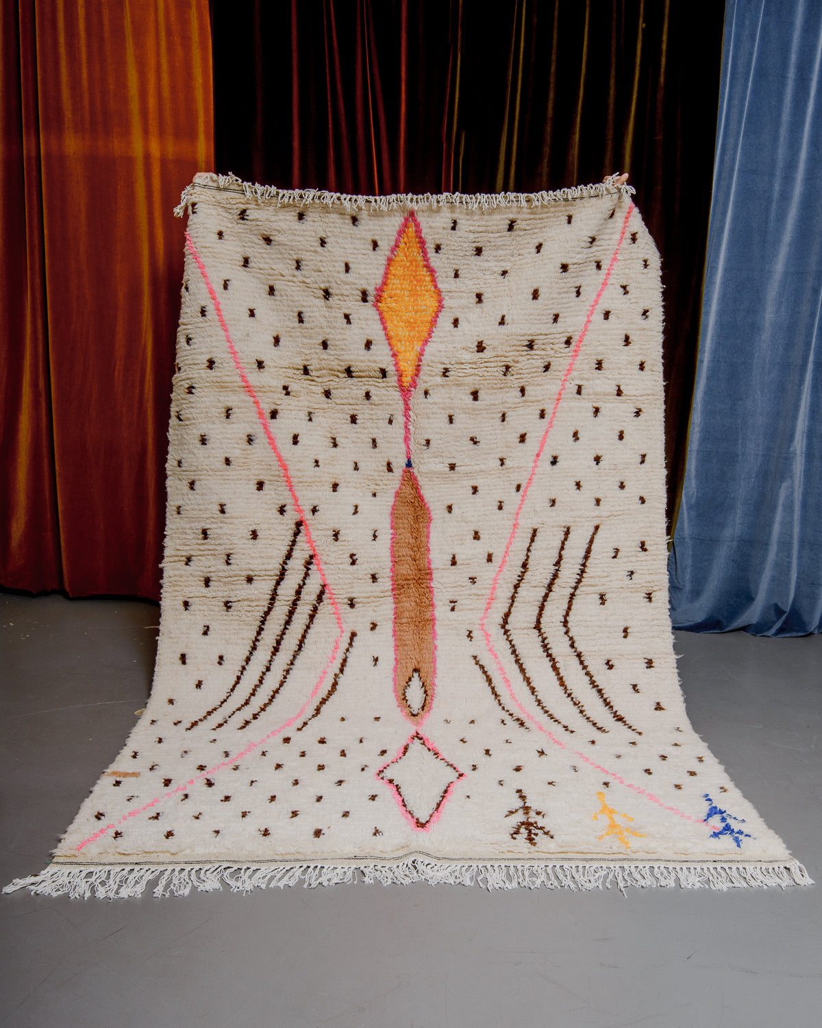 Azilal rug held in front of velvet curtains. 