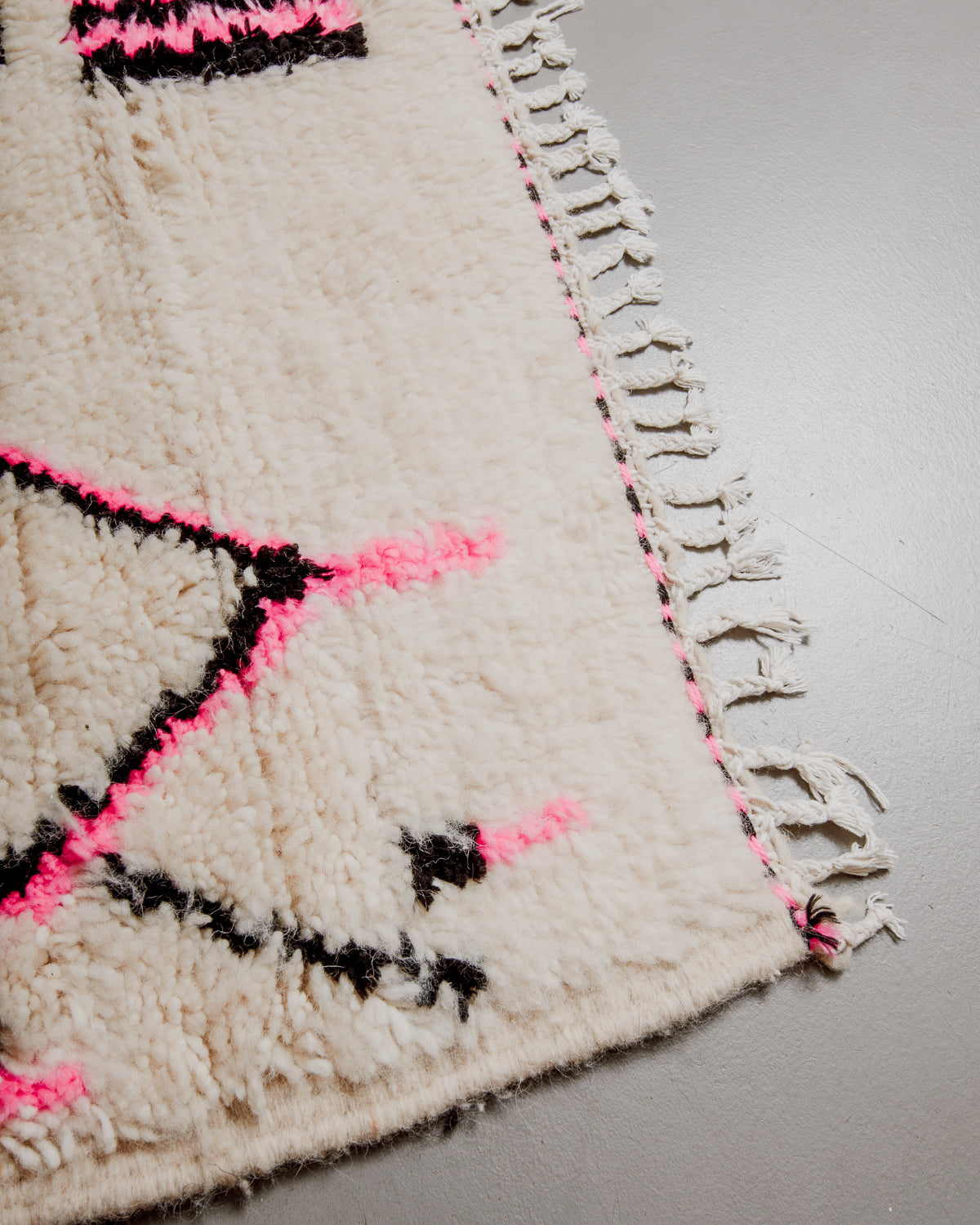 Corner of azilal rug with pink and black stitching along the end and white cotton tassels. 