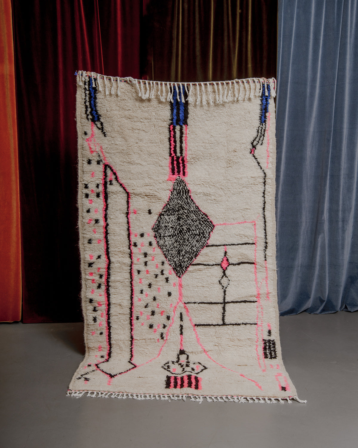 Colourful azilal rug held in front of velvet curtains. 