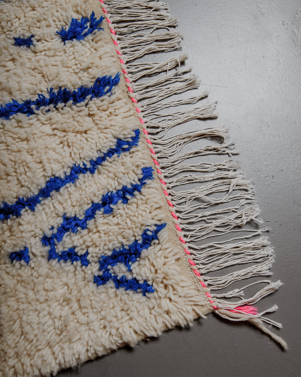 Corner of azilal rug with pink and white stitching along the end and white cotton tassels. 
