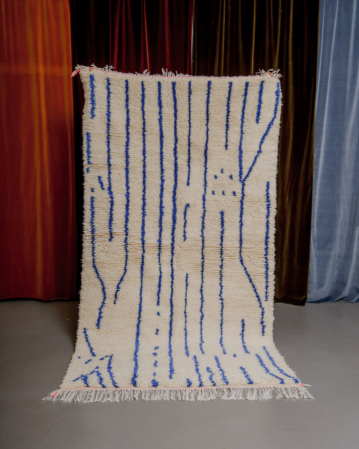 Colourful azilal rug held in front of velvet curtains. 