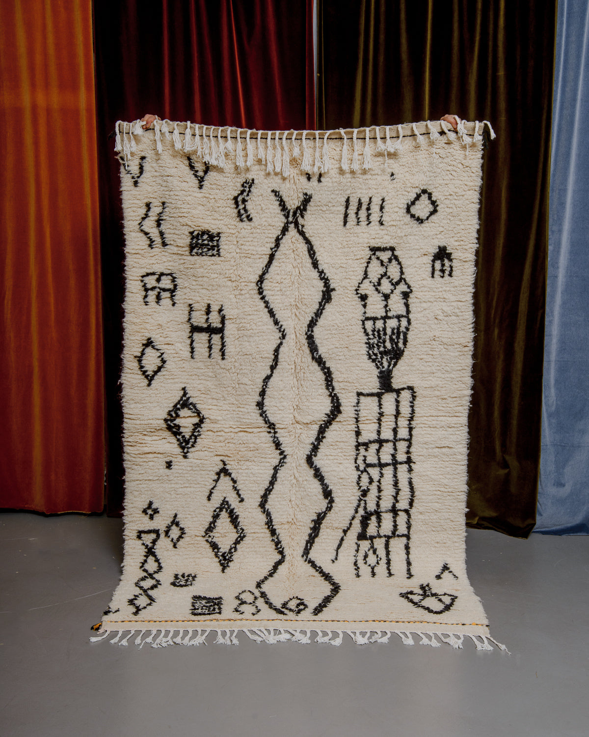 Azilal rug held in front of velvet curtains. 