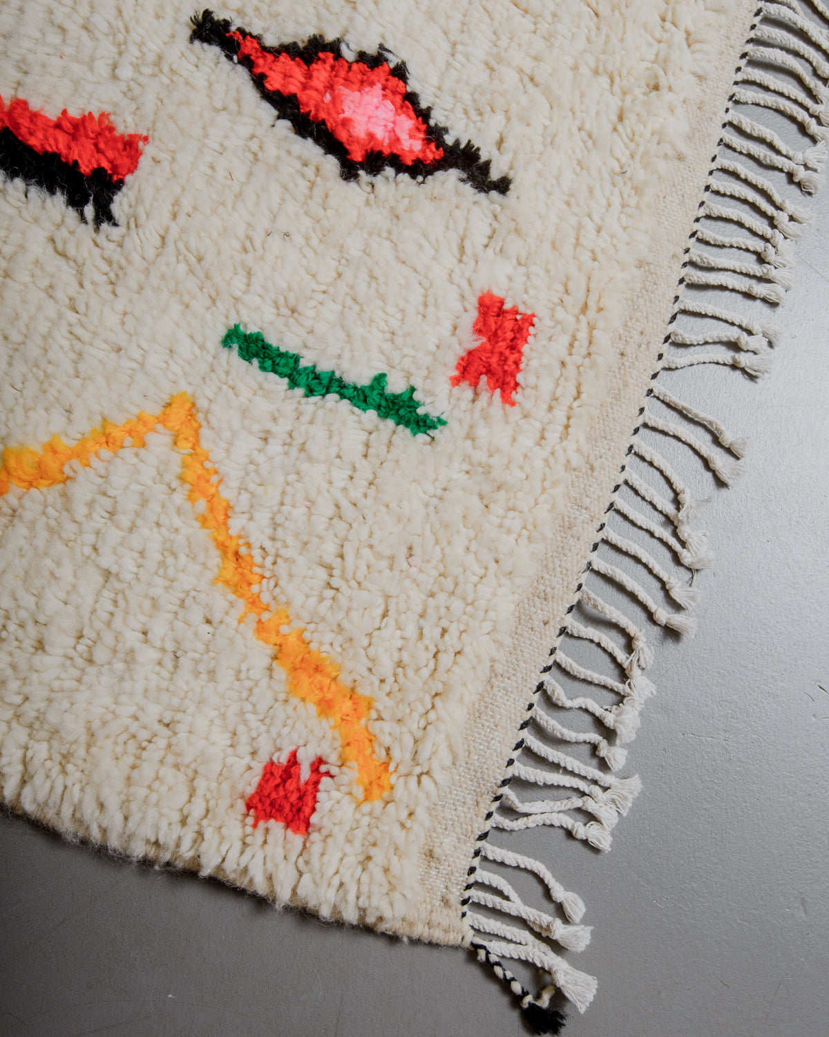 Corner of azilal rug with black and white stitching along the end and white cotton tassels. 