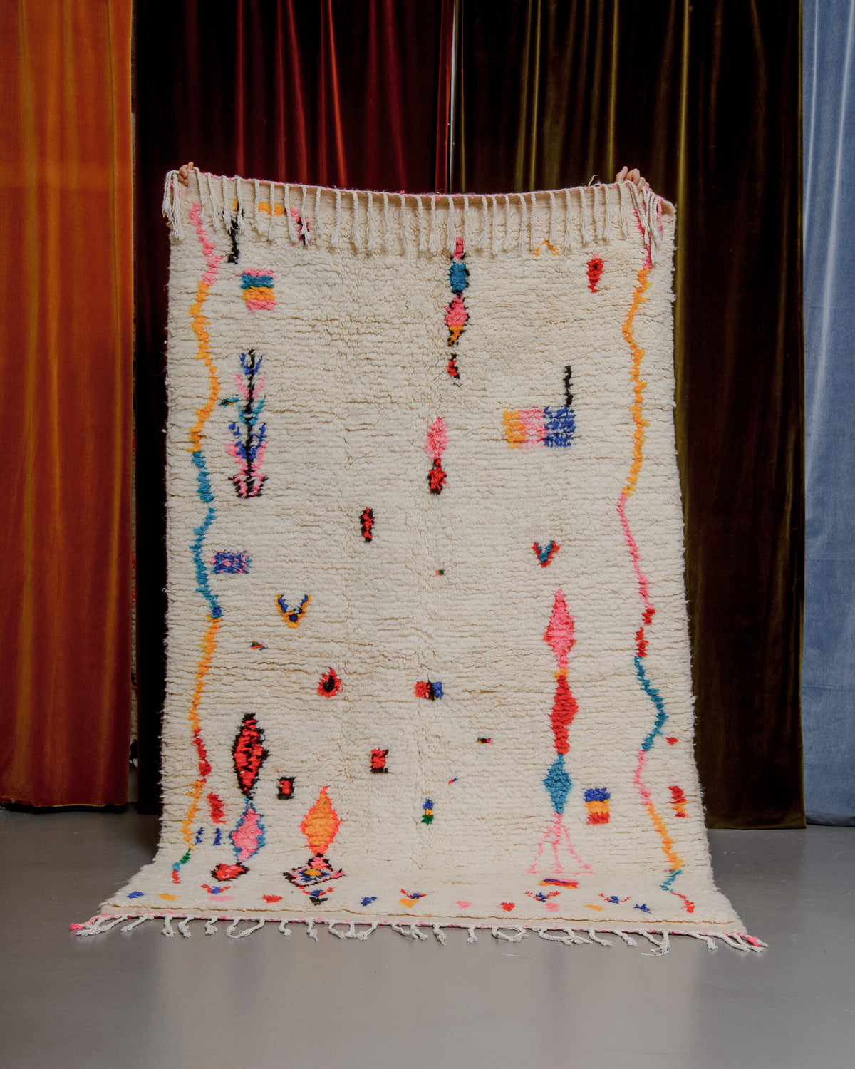 Azilal rug held in front of velvet curtains. 