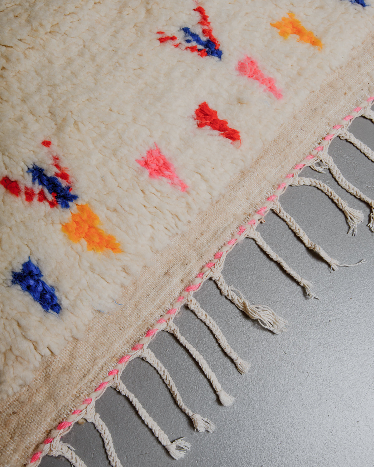 Edge of azilal rug with pink and white stitching along the end and white cotton tassels. 