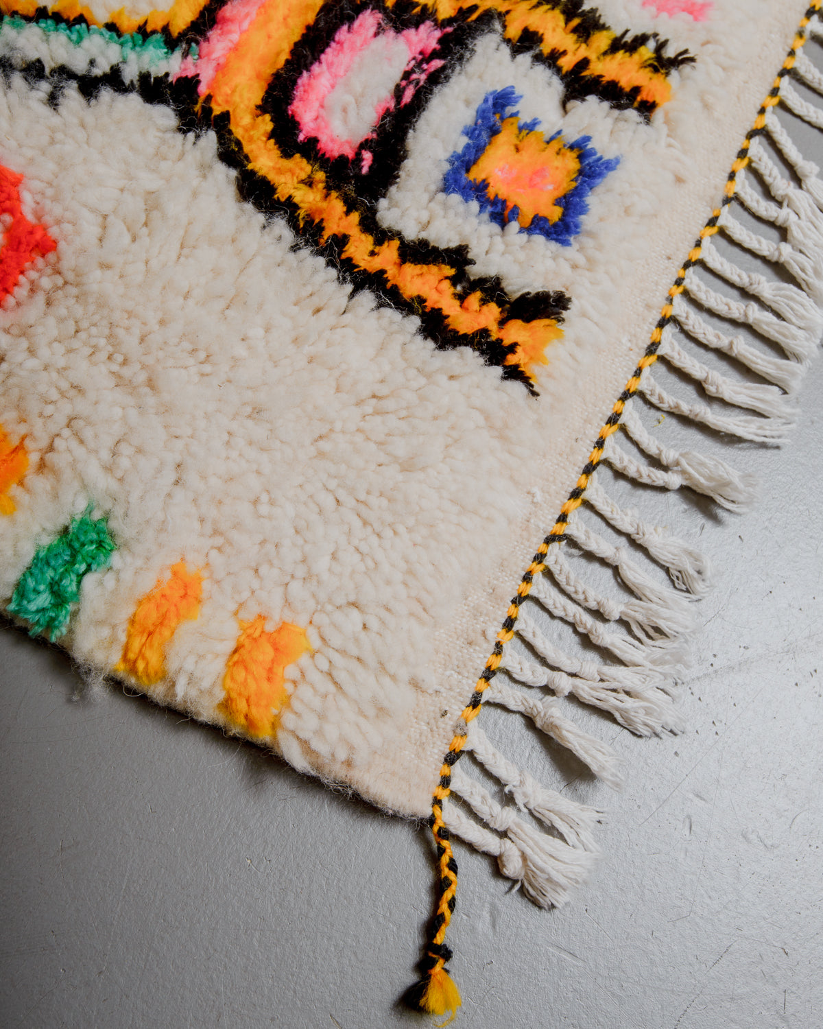 Edge of azilal rug with yellow and black stitching along the end and white cotton tassels. 