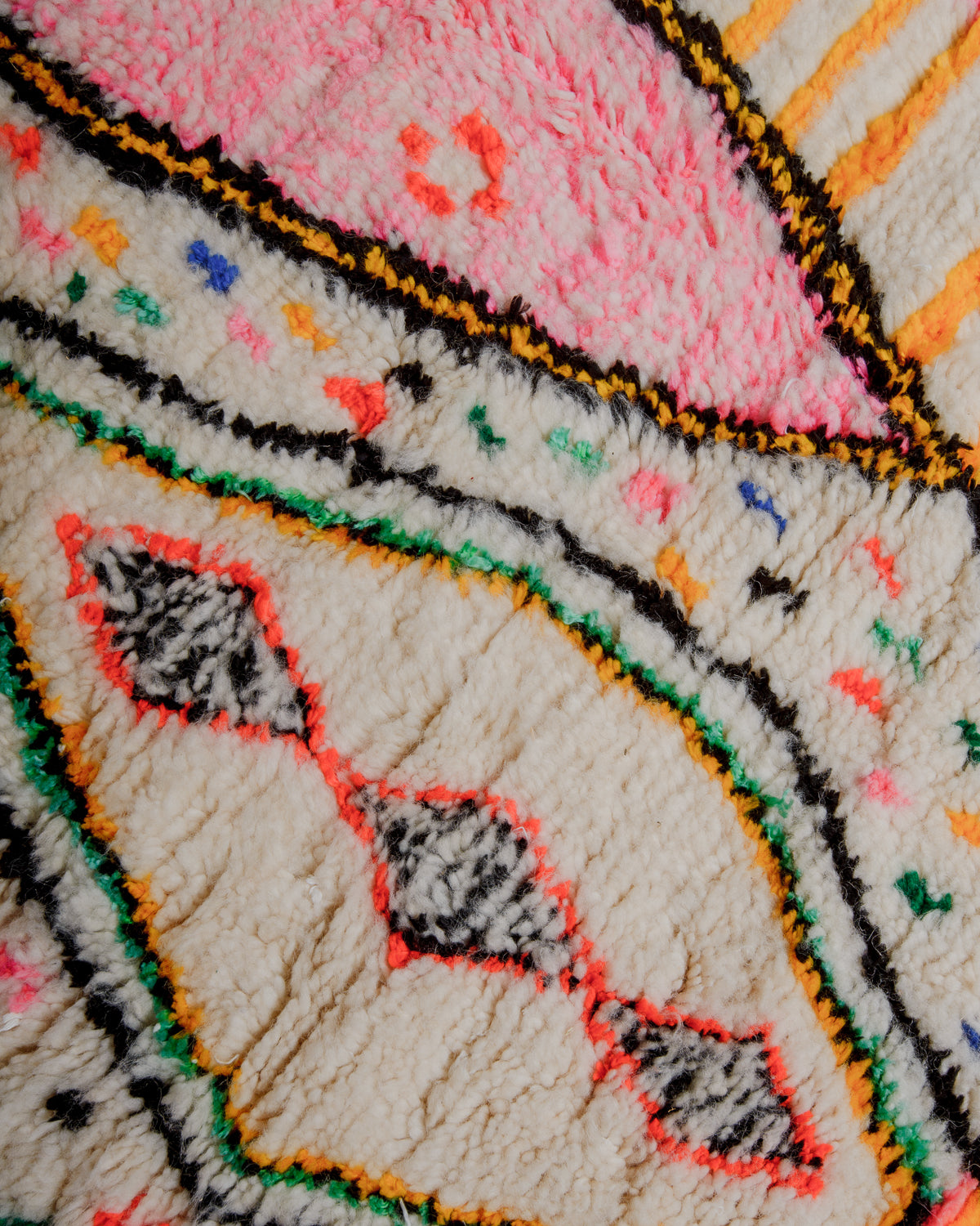Surface of colourful azilal rug with cream wool and cotton details in pink, yellow, green, orange and black.