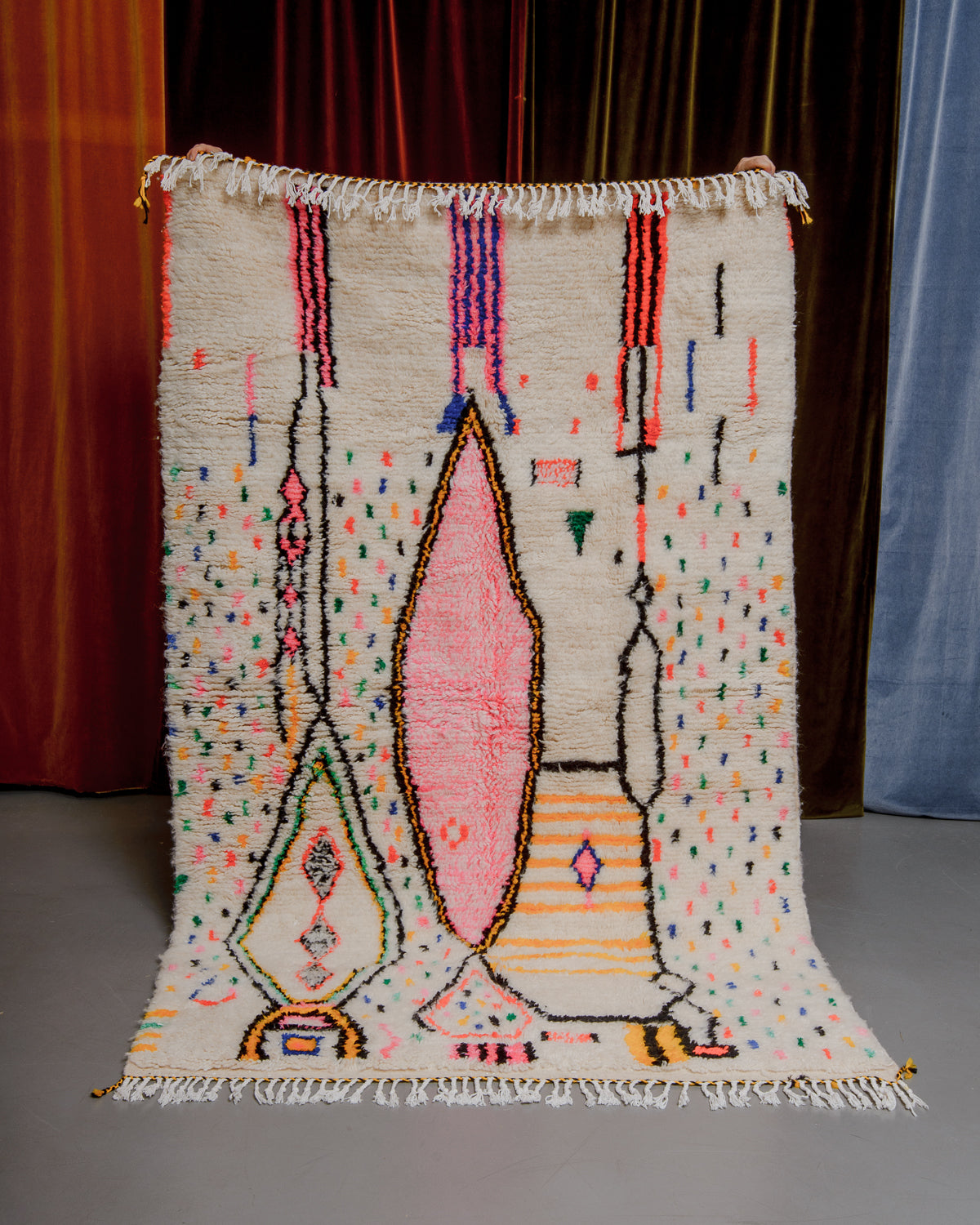 Azilal rug held in front of velvet curtains. 
