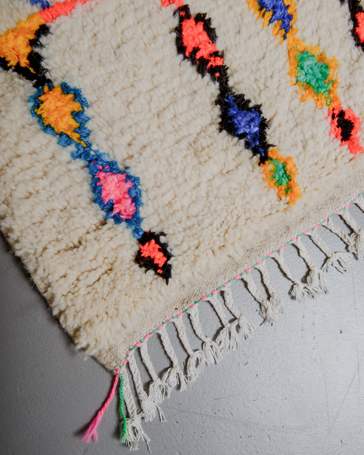 Edge of azilal rug with pink and green stitching along the end and white cotton tassels. 