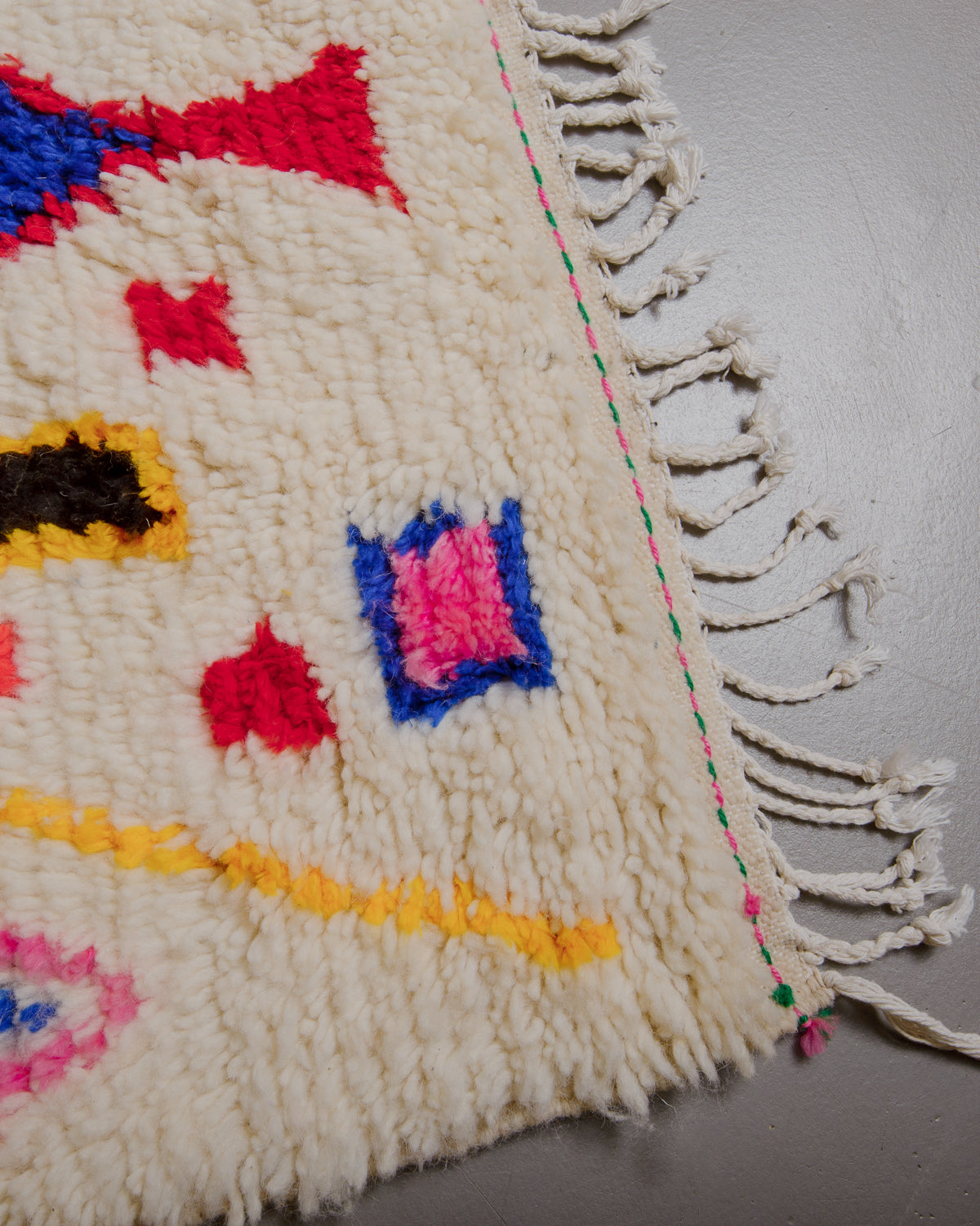 Corner of Berberlin azilal rug with green and pink stitching along the woven edge and white cotton tassels.