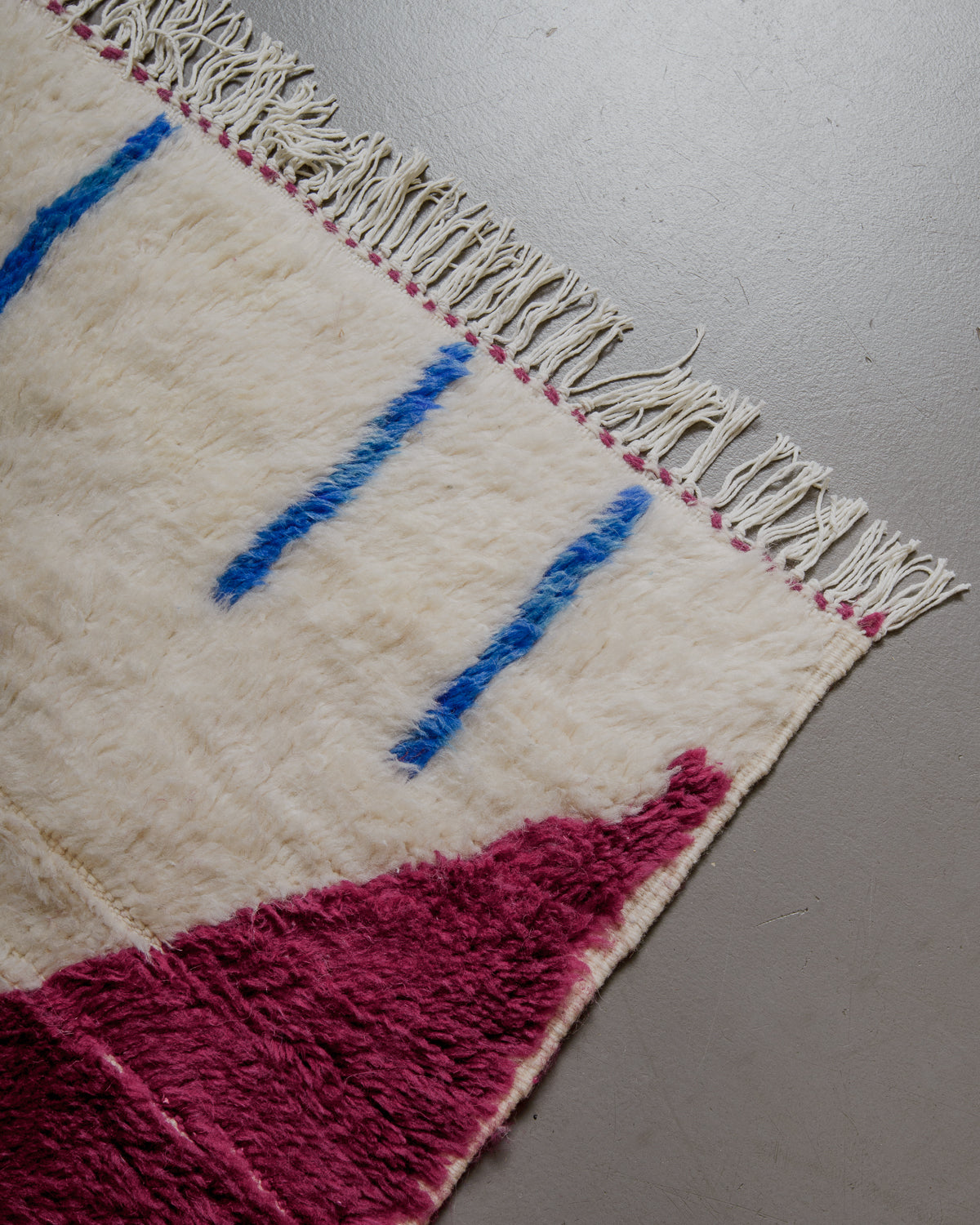 Colourful woven rug with geometric patterns and a white fringe on a neutral background.