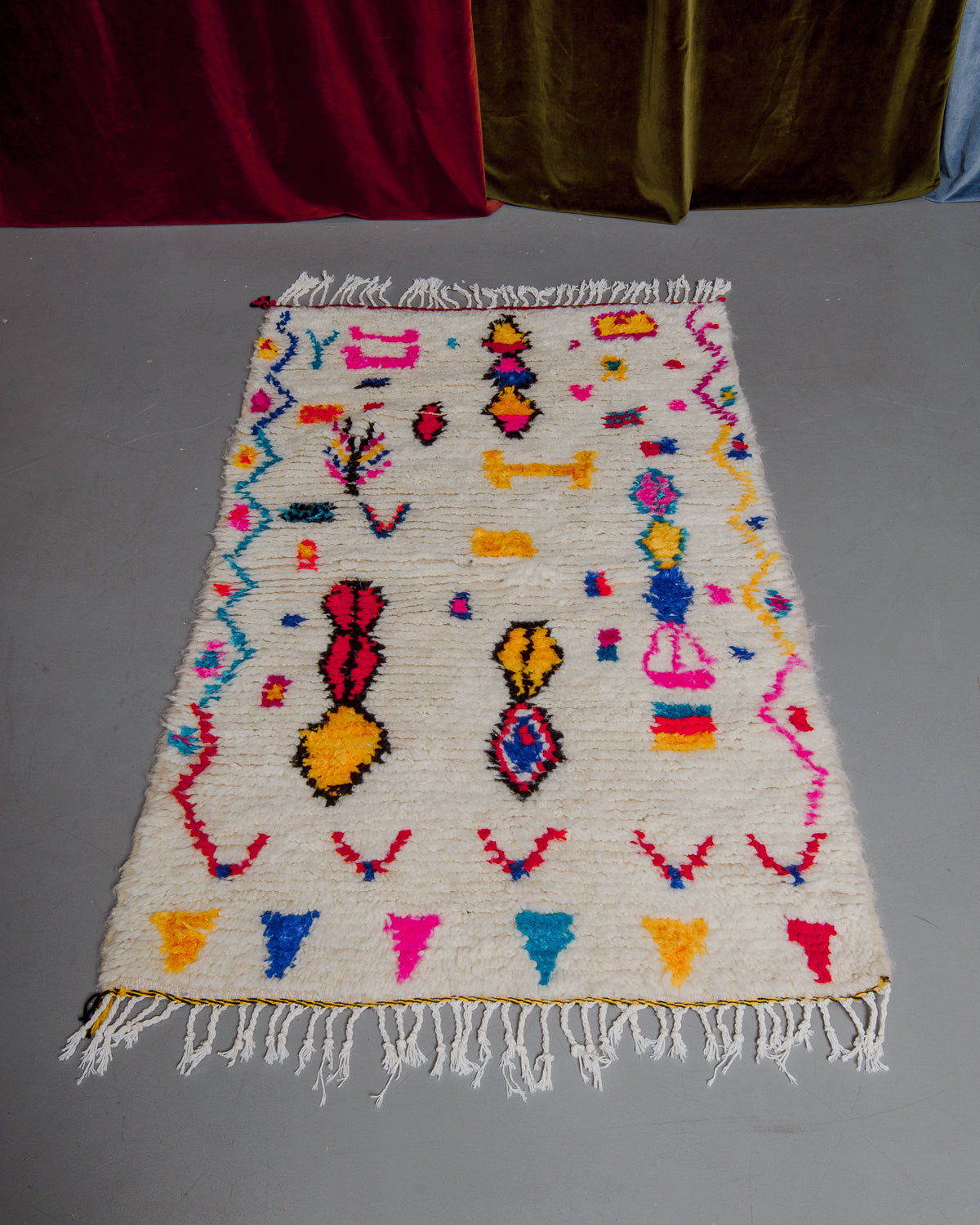 Azilal rug featuring colourful design on a grey floor in front of curtains.