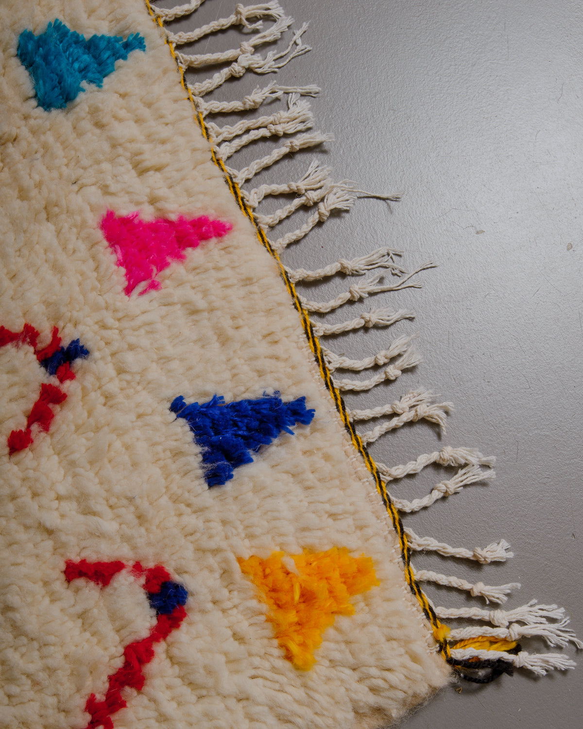 Edge of azilal rug with yellow and black stitching along the end and white cotton tassels. 