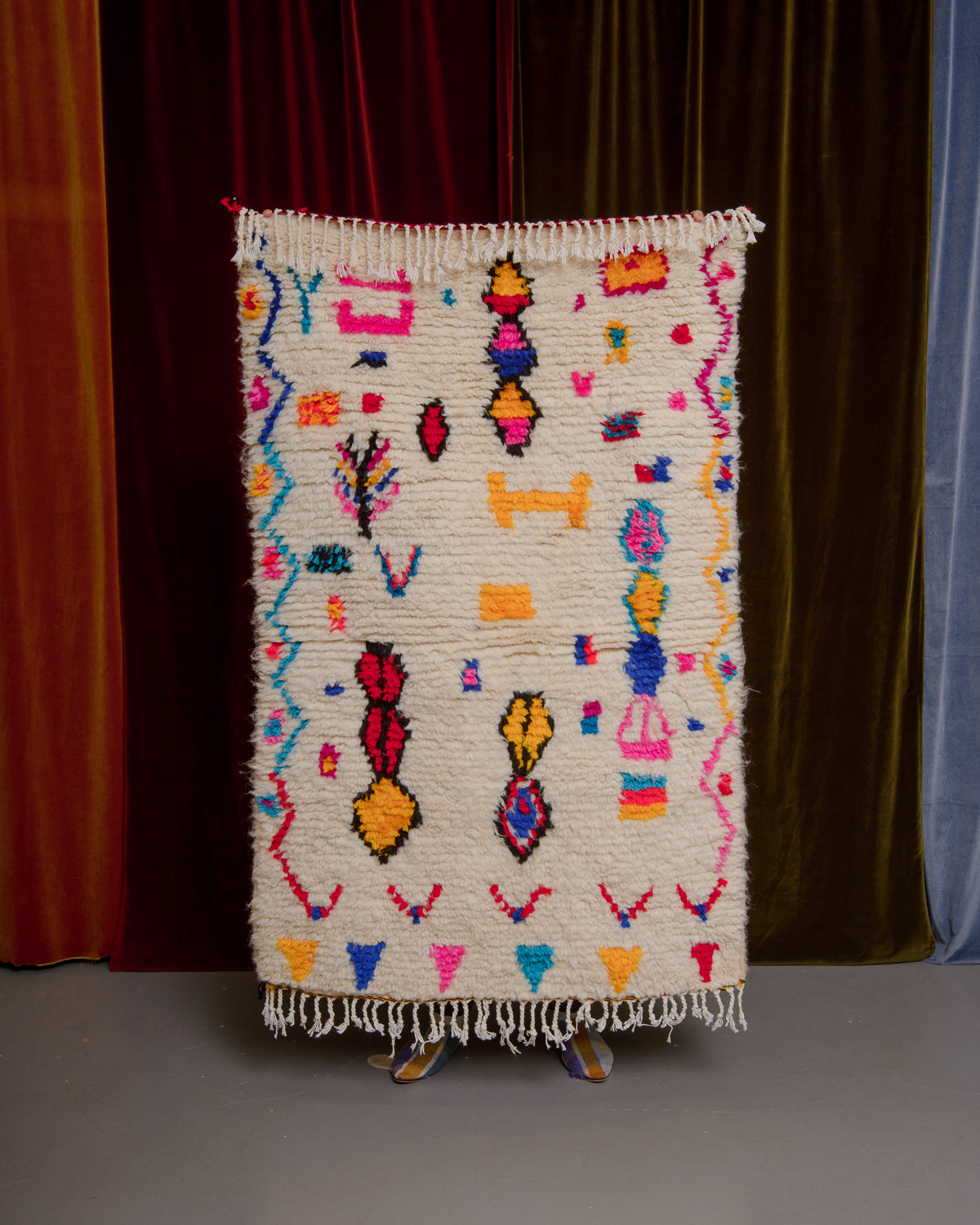 Azilal rug held in front of velvet curtains. 