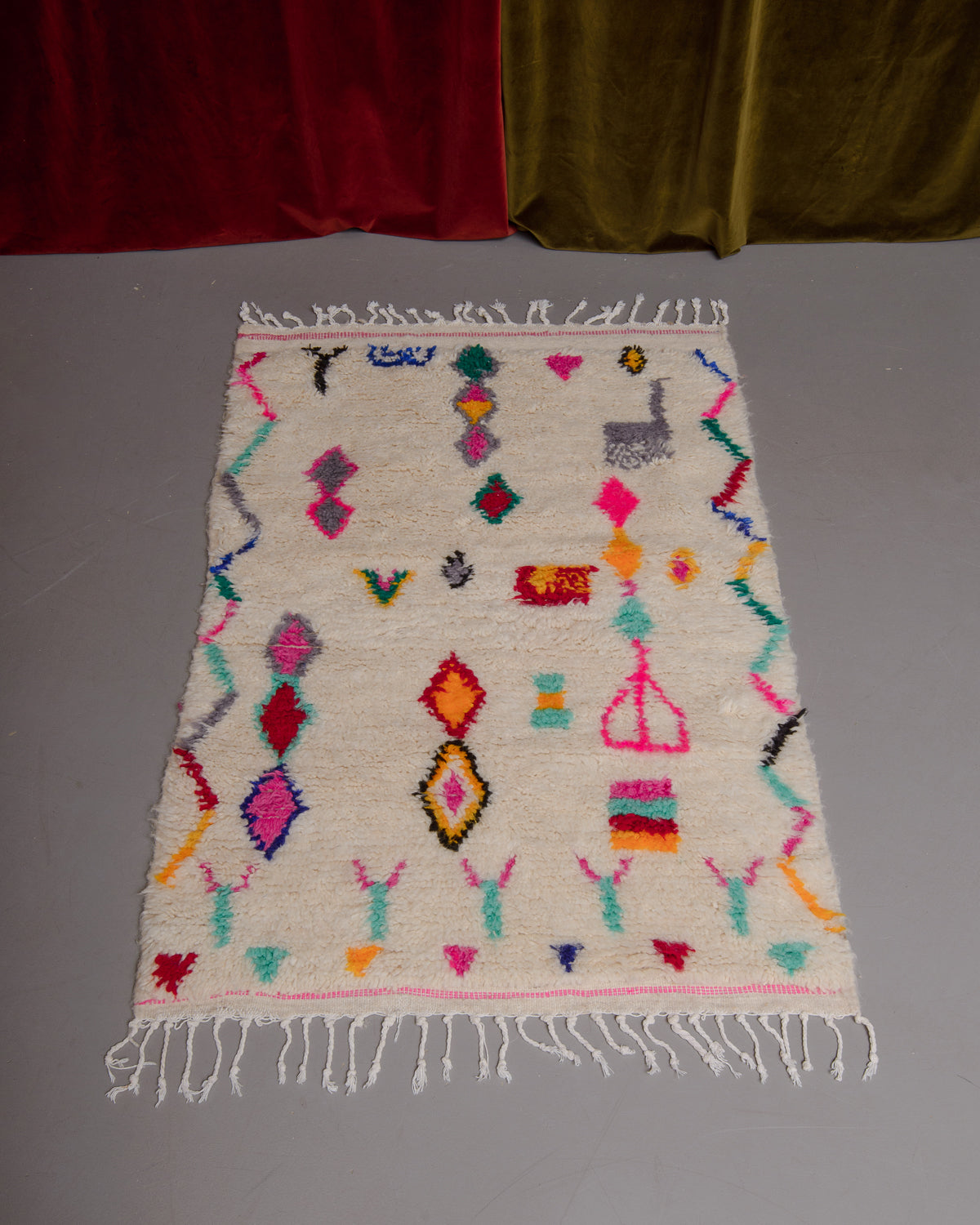 Azilal rug featuring colourful design on a grey floor in front of curtains.