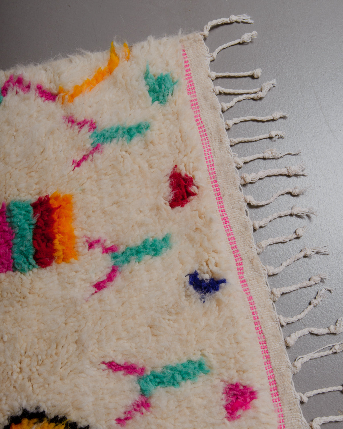 Edge of azilal rug with pink stitched design across the end and white cotton tassels. 